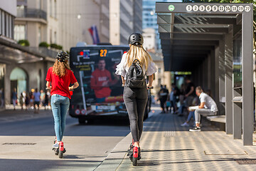 Image showing Rear view of trendy fashinable teenager girls riding public rental electric scooters in urban city environment. New eco-friendly modern public city transport in Ljubljana, Slovenia