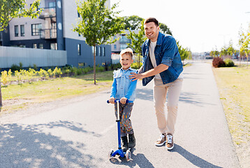 Image showing happy father and little son riding scooter in city