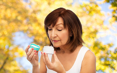 Image showing senior woman with cream jar over autumn trees