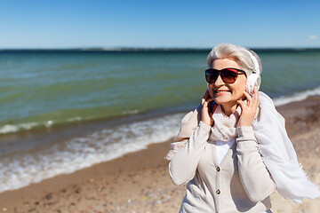 Image showing old woman in headphones listens to music on beach