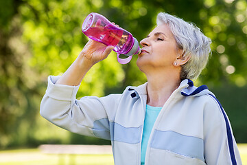 Image showing senior woman drinks water after exercising in park