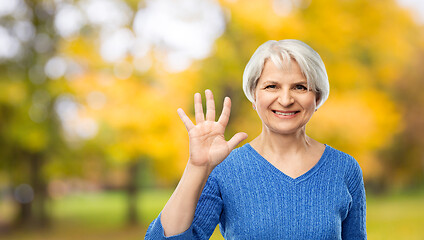 Image showing smiling senior woman showing palm in autumn park