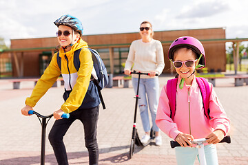 Image showing happy school children with mother riding scooters