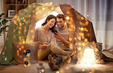 Image showing happy couple with smartphone in kids tent at home