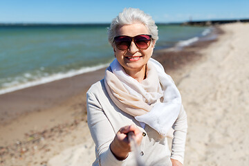 Image showing old woman taking picture by selfie stick on beach