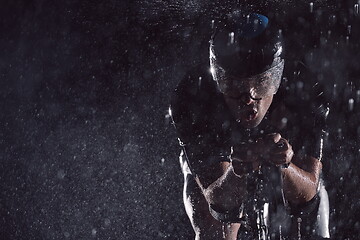 Image showing triathlon athlete riding bike fast on rainy night