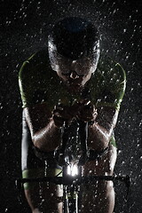 Image showing triathlon athlete riding bike fast on rainy night