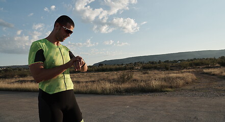 Image showing triathlon athlete resting and setting smartwatch