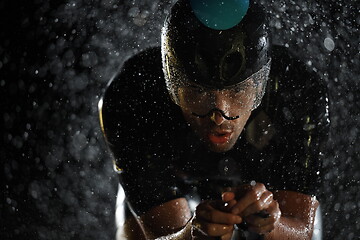 Image showing triathlon athlete riding bike fast on rainy night