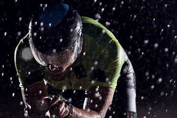 Image showing triathlon athlete riding bike fast on rainy night