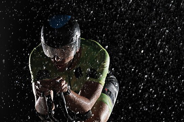 Image showing triathlon athlete riding bike fast on rainy night