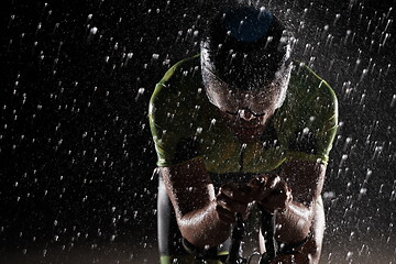 Image showing triathlon athlete riding bike fast on rainy night