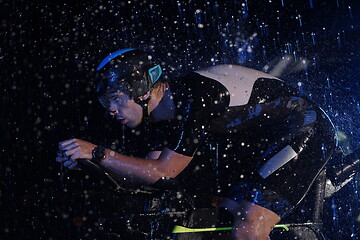 Image showing triathlon athlete riding bike fast on rainy night