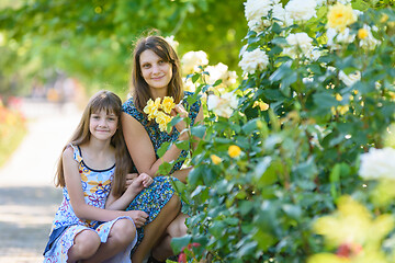 Image showing mom and daughter sit in the park near the bush with roses