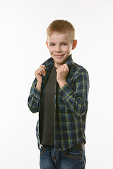 Image showing blond boy on a white background holds hands behind the collar of a checkered shirt