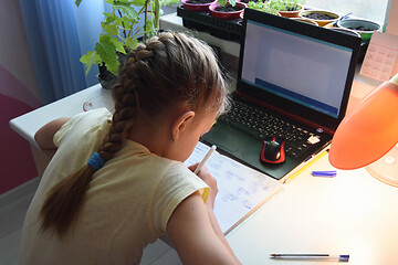 Image showing Girl solves math examples in notebook in front of laptop