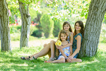 Image showing Mom with two daughters sits on green grass near tree in park
