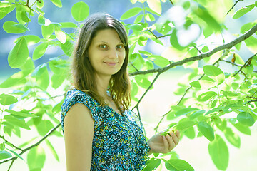 Image showing Girl smiles against a branch with green leaves in sunny weather
