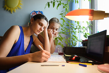 Image showing Mother solves daughter\'s assignments to study in notebooks at home at the desk