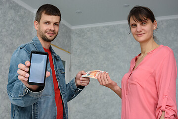 Image showing A self-employed man receives money from a girl for repairing a room and shows a phone with the mobile application