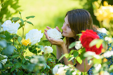 Image showing Young girl enjoys the scent of roses in the park