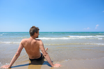 Image showing A man sits on the seashore and looks into the distance