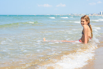 Image showing A girl of ten years old sits in the water on an empty seashore