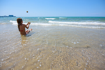 Image showing Girl sitting on the seashore and throws sand balls