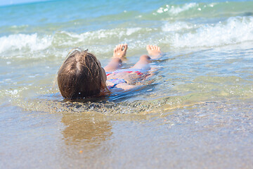 Image showing A girl lies on her back in shallow water on the sea sandy coast