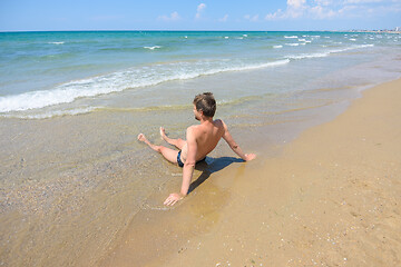 Image showing A man sits on an empty sandy sea beach in the water