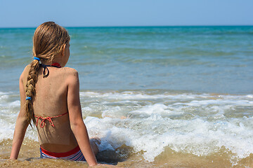 Image showing A girl sits on a sandy sea beach and looks into the distance