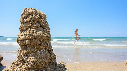 Image showing A pile of wet sand on the seashore, on the right there is an empty place for inscription, in the background a girl runs