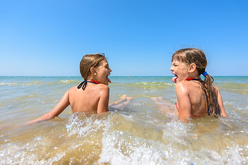 Image showing Children sit together in shallow water and show each other tongue