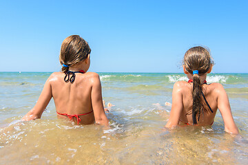 Image showing Children sit in the water on the coast and look into the distance