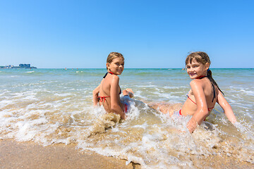 Image showing Two girls sit on the sea coast and turn around happily looking at the frame