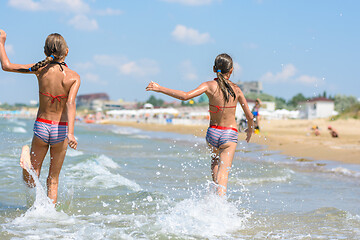 Image showing Two girls joyfully run along the sea on a warm summer day, rear view