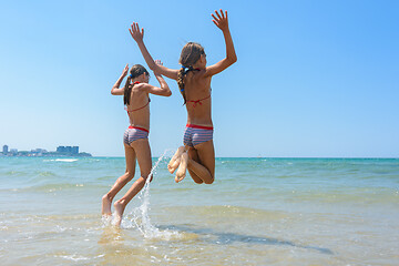 Image showing Two girls joyfully bounce on the seashore