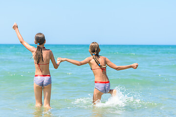 Image showing Sisters joyfully and happily run into the sea on a hot sunny day