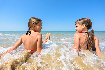 Image showing Children sit in water on a sandy beach and look at each other happily