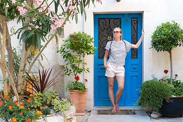 Image showing Beautiful young female tourist woman wearing sun hat, standing and relaxing in shade in front of vinatage marine blue wooden door in old Mediterranean town while sightseeing on hot summer day