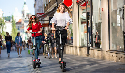 Image showing Trendy fashinable teenager girls riding public rental electric scooters in urban city environment. New eco-friendly modern public city transport in Ljubljana, Slovenia