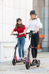 Image showing Trendy fashinable teenager girls riding public rental electric scooters in urban city environment. New eco-friendly modern public city transport in Ljubljana, Slovenia