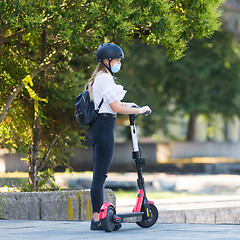 Image showing Trendy fashinable teenager girl wearing corona virus protective face mask in public while using rental electric scooters in city environment. New eco-friendly city transport in Ljubljana, Slovenia