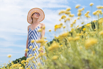 Image showing Young woman wearing striped summer dress and straw hat standing in super bloom of wildflowers, relaxing while enjoing beautiful nature of of Adriatic sea coastal nature of Croatia.