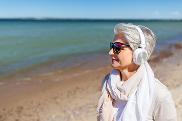 Image showing old woman in headphones listens to music on beach