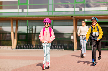 Image showing happy school children with mother riding scooters