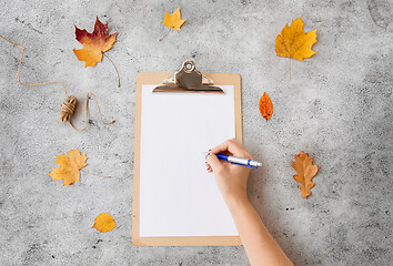 Image showing hand writing on white paper on clipboard in autumn