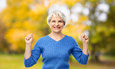 Image showing happy old woman celebrating success in autumn park