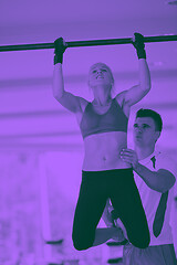 Image showing trainer support young woman while lifting on bar in fitness gym