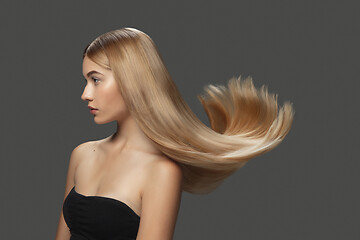 Image showing Beautiful model with long smooth, flying blonde hair isolated on dark studio background.